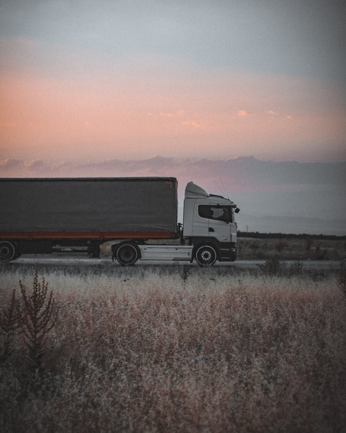 pexels photo 5410923 A cargo truck travels on a highway at sunset, surrounded by an open landscape, symbolizing logistics and transportation.